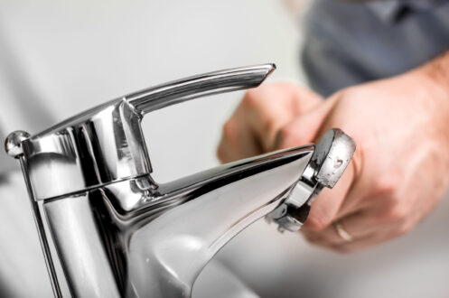 A person uses a wrench to tighten or repair a chrome bathroom faucet.