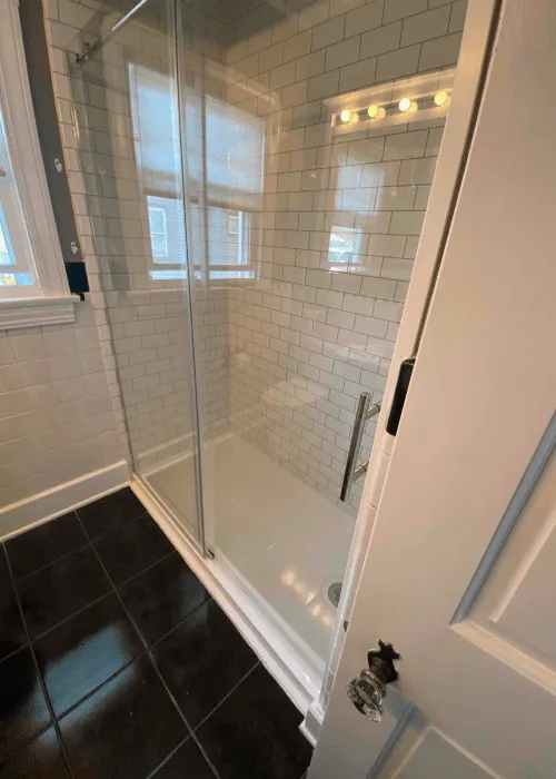 A bathroom with a black tiled floor, glass-enclosed shower with white subway tile walls, and a vanity light above the shower—perfect inspiration for any Photo Gallery.
