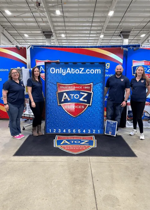 Four people stand in front of an "A to Z Services" promotional display at an indoor event, with OnlyAtoZ.com visible above the logo—a great addition to any event photo gallery.