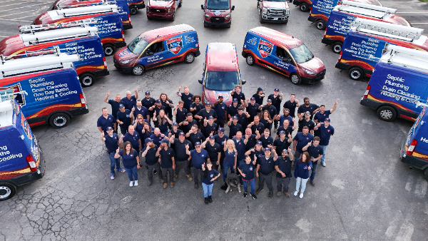 A large group of people stands in a parking lot surrounded by blue and red service vans with company logos.