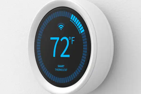 A round smart thermostat mounted on a wall displays 72°F with a blue digital interface and Wi-Fi signal icon.