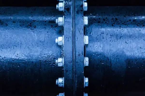 Close-up view of two large black metal pipes joined together with bolts, showing textured surfaces and blue-tinted lighting.
