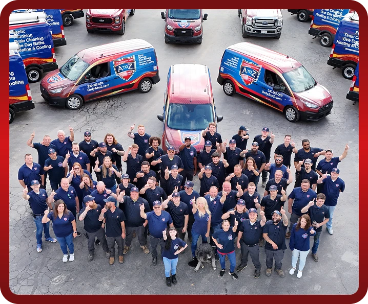 A large group of uniformed workers stands in a parking lot, surrounded by company vans with A to Z branding; most people are smiling and raising a finger.